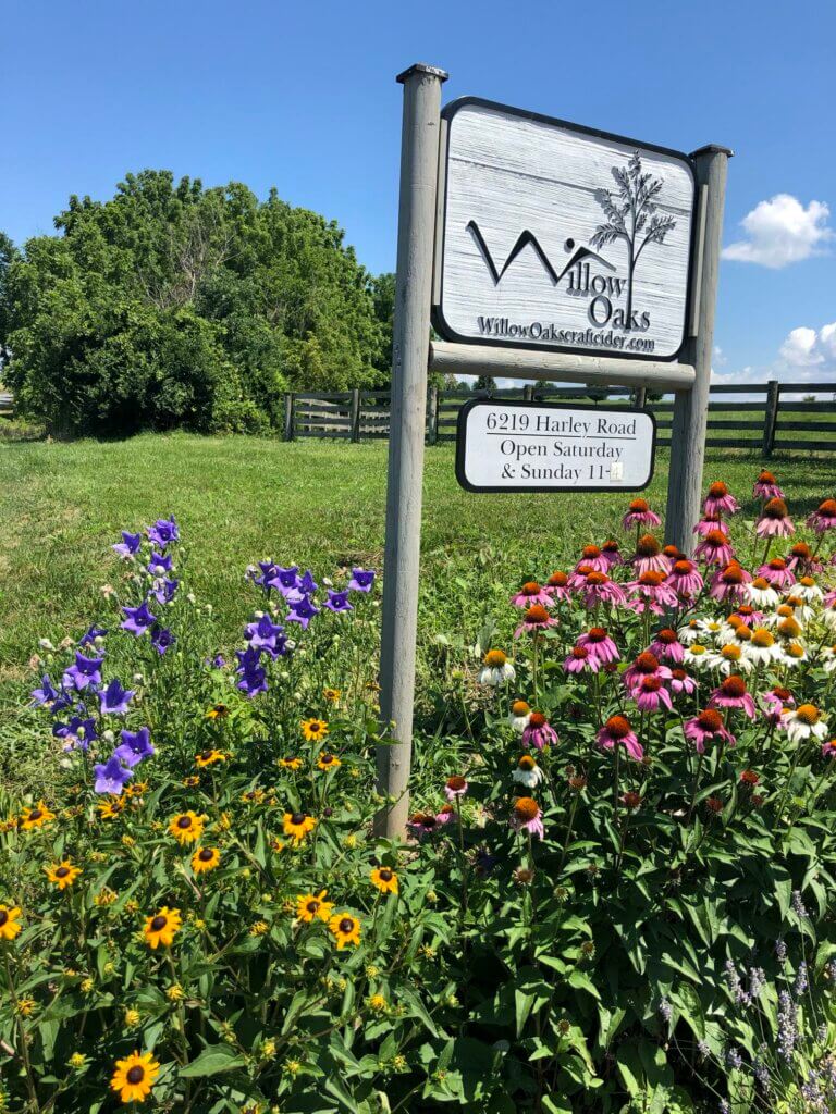 Willow Oaks craft cider road sign at entrance surrounded by spring flowers