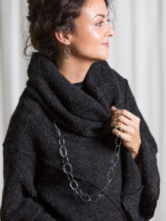 Photo: A woman in a black cowl-neck sweater wears a necklace and earrings made from large hand-wrought metal links.