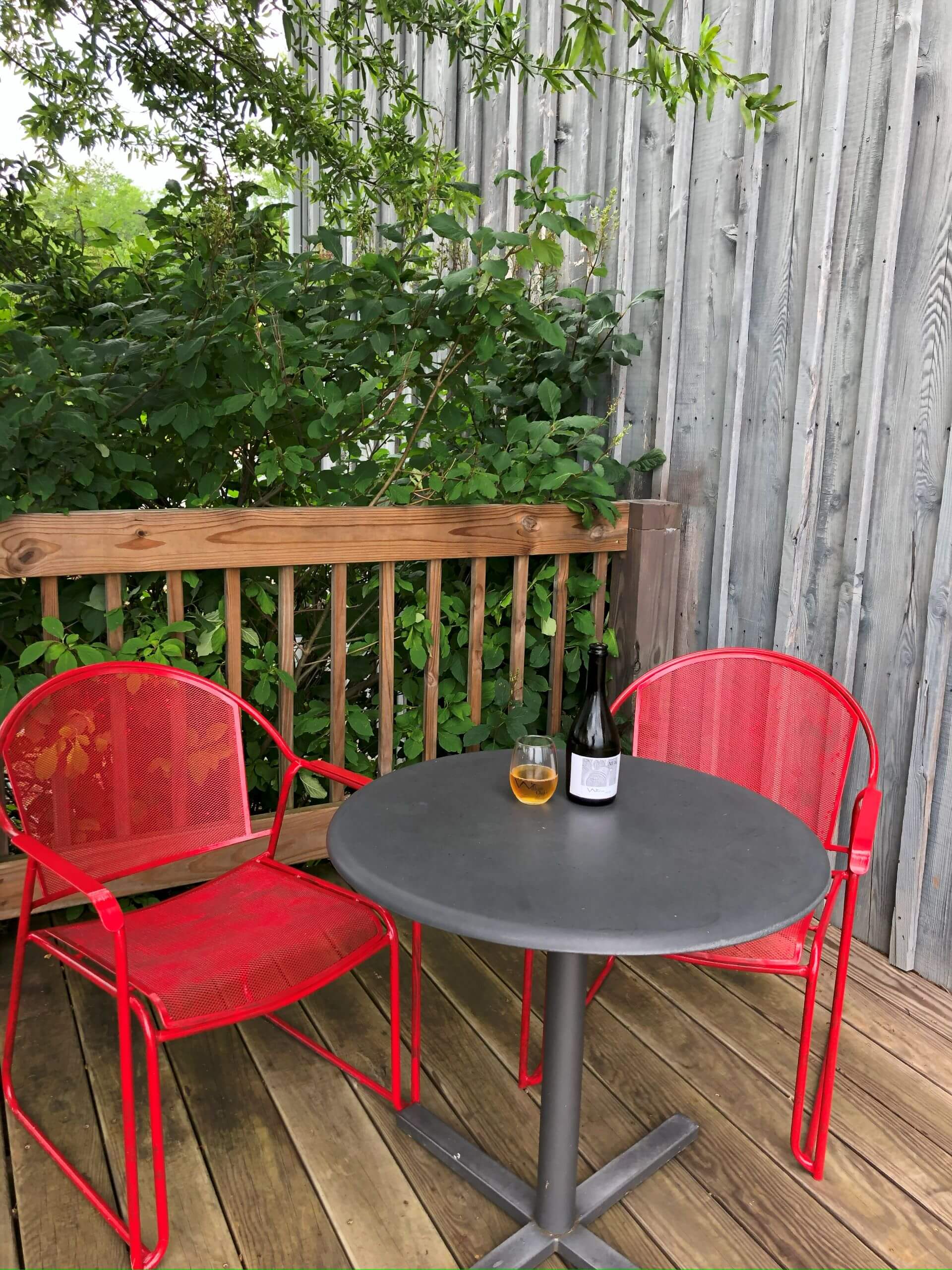 An outdoor dining set with two red chairs and a round cafe table on the deck at Willow Oaks craft cider.
